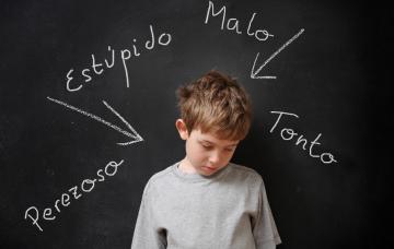 Etapas de la hiperactividad o TDAH Niño con hiperactividad o TDAH delante de una pizarra con descalificativos