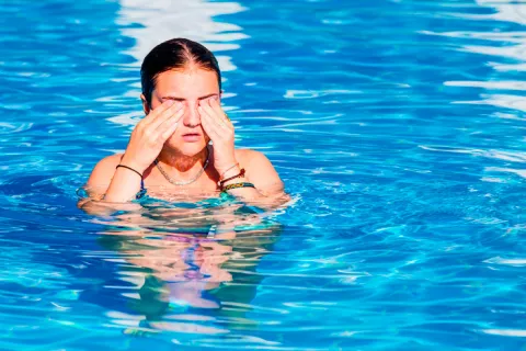 Una joven en la piscina se frota los ojos