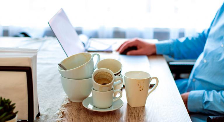 Trabajador con muchas tazas de café junto a su ordenador