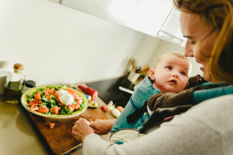 Medre cocinando junto a su bebé con gesto relajado y feliz