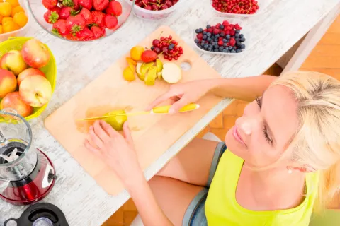 Una mujer corta frutas con la intención de preparar un batido