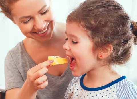 Madre da de comer queso a su hija pequeña