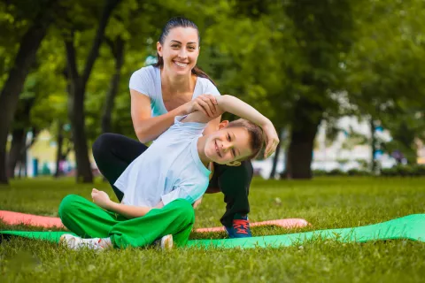 Un niño practica yoga en un parque con la ayuda de su profesora