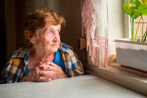 Mujer mayor mira por la ventana con gesto triste