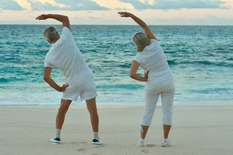 Una pareja de adultos mayores hace gimnasia en la playa al atardecer