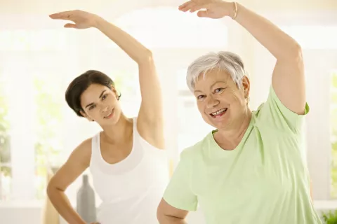 Una anciana hace yoga junto a su monitora