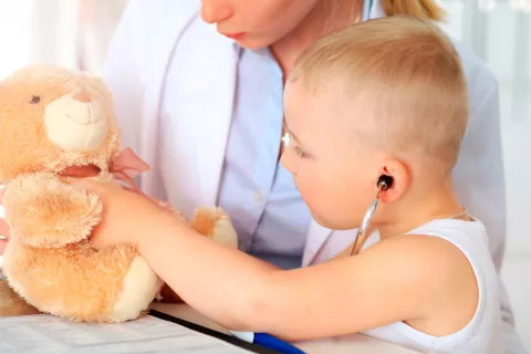 Un niño pequeño ausculta a su osito de peluche en presencia de su doctora