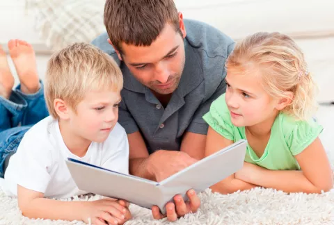 Un padre y sus dos hijos leen un libro