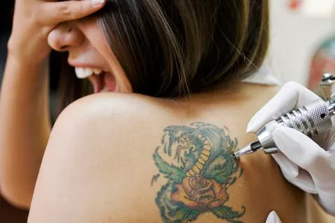 Una joven se queja mientras le realizan un tatuaje en la espalda