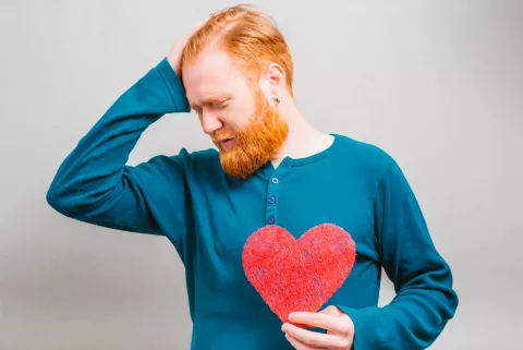 Un hombre sujeta un corazón con una mano, mientras se sujeta la cabeza con gesto de preocupación