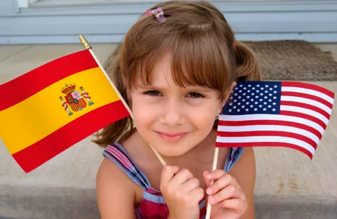 Niña sosteniendo una bandera española y otra estadounidense