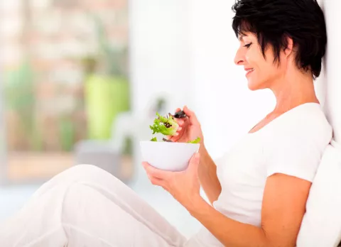 Una mujer de mediana edad lee un libro de recetas en la cocina