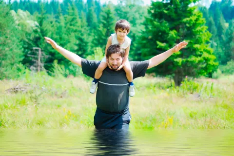 Un hombre cruza un arroyo con su hijo a hombros