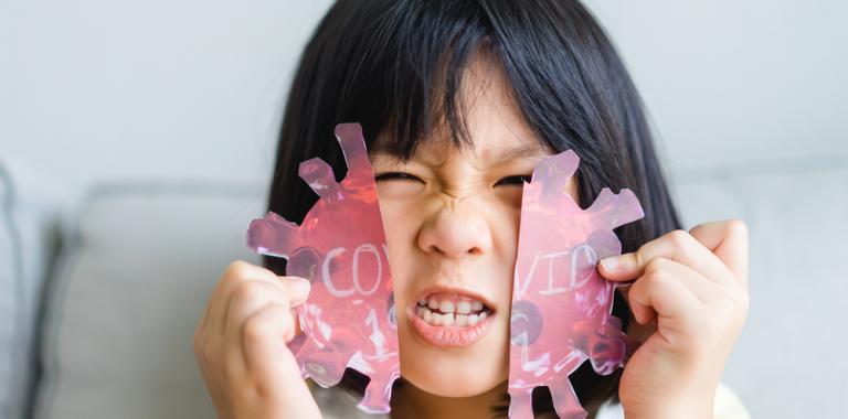 Niño rompiendo una silueta del virus COVID-19 hecha en papel