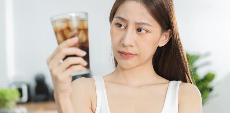 Una mujer joven mirando con desconfianza un vaso con un refresco de cola