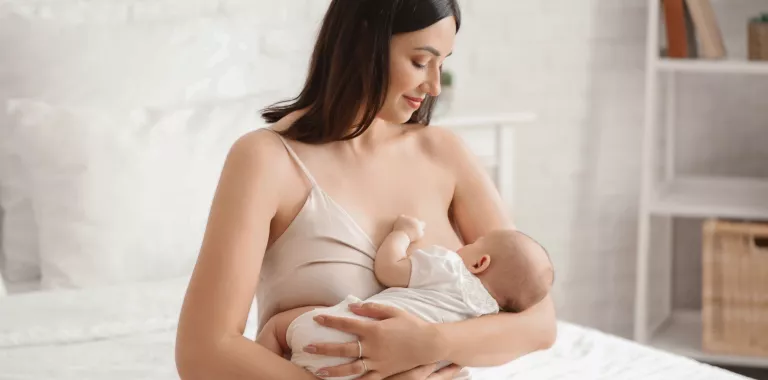 Mujer alimenta a su bebé con lactancia materna Mujer joven amamanta a su bebé sentada sobre la cama