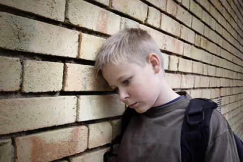 Niño triste con la cabeza apoyada en una pared