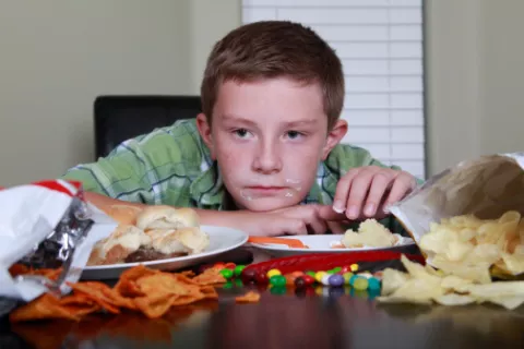 Niño sentado a la mesa rodeado de alimentos inadecuados