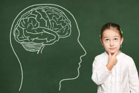 Niña junto a una pizarra con un dibujo de un cerebro humano