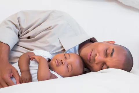 Un padre y su bebé durmiendo en el sofá