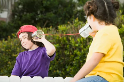 Dos niños juegan a hablarse a través de dos botes de conserva vacíos