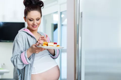 Mujer embarazada sale de la cocina con un plato de pasteles en la mano