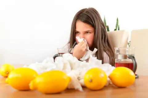 Una joven se suena junto a una mesa con limones