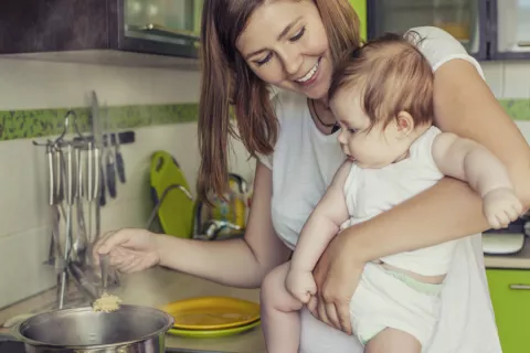 Una madre prepara la comida con su bebé en brazos