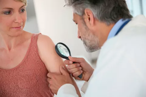 Un dermatólogo examina la piel del brazo de una paciente