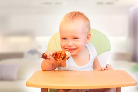 Un niño pequeño muerde un muslo de pollo