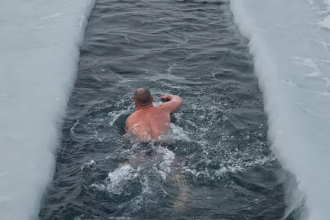 Un hombre nada en una piscina rodeado de nieve