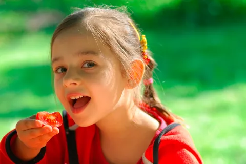 Una niña a punto de comerse un trozo de tomate