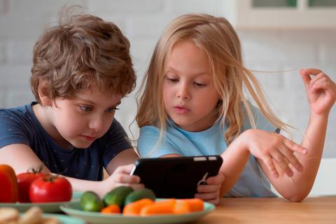 Hermanos pequeños jugando co el móvil en la cocina