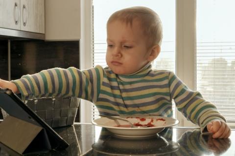 Niño pequeño enfadado junto a una tablet y un plato de comida