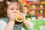 Obesidad infantil Niña con obesidad infantil comiendo una hamburguesa