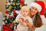 Comidas navideñas con bebés: qué debemos evitar Madre sosteniendo a su bebe comiendo junto al árbol de navidad