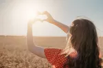En España nos falta vitamina D: por qué la necesitas y cómo evitar su déficit Mujer frente al sol haciendo el gesto de un corazón con las manos