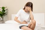 Mujer sentada en la cama con fuertes dolores premenstruales