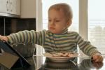 Niño pequeño enfadado junto a una tablet y un plato de comida