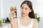 Una mujer joven mirando con desconfianza un vaso con un refresco de cola