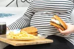 Dieta occidental rica en grasas y azúcares en el embarazo aumenta el riesgo de TDAH en el hijo Embarazada se dispone a tomar hamburguesas, patatas fritas y refresco de cola