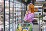 Alimentos enriquecidos o fortificados en los estantes del supermercado Mujer pelirroja en el supermercado dudando que alimento escoger