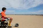 Niño con distrofia muscular de Duchenne en silla de ruedas en la playa Niño en silla de ruedas sobre la arena de la playa