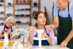 Taller de manualidades donde un hombre mayor da clases Hombre mayor explica a una joven cómo hacer productos de arcilla