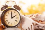 Un reloj junto a una manta y unas hojas caídas simboliza el cambio al horario de invierno Reloj despertador junto a manta y hojas otoñales