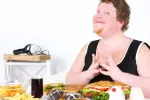 Alimentos sobre una mesa junto a un joven con obesidad Hombre obeso sentado a una mesa repleta de alimentos