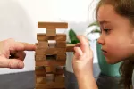 Padre e hija jugando con torre de madera de la jenga Niña juega con su padre a la jenga quitando una pieza de madera